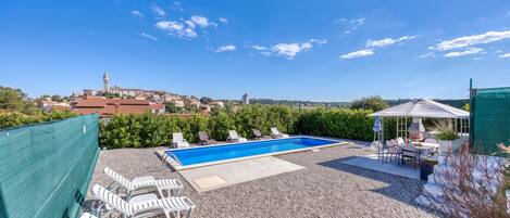 A rooftop pool with lounge chairs, a barbecue area, and a view of a town with a church tower.