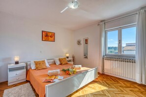 Un dormitorio con cama, mesitas de noche, un ventanal con vistas y un ventilador de techo.