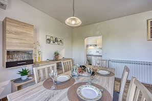 A dining area with a wooden table set for four, a hanging light fixture, and a kitchen in the background. - Pool House Lilly (Visnjan)