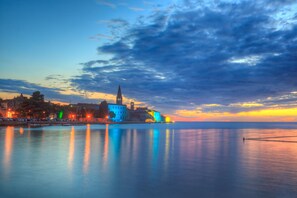 A waterfront cityscape at dusk with illuminated buildings reflecting on calm water.