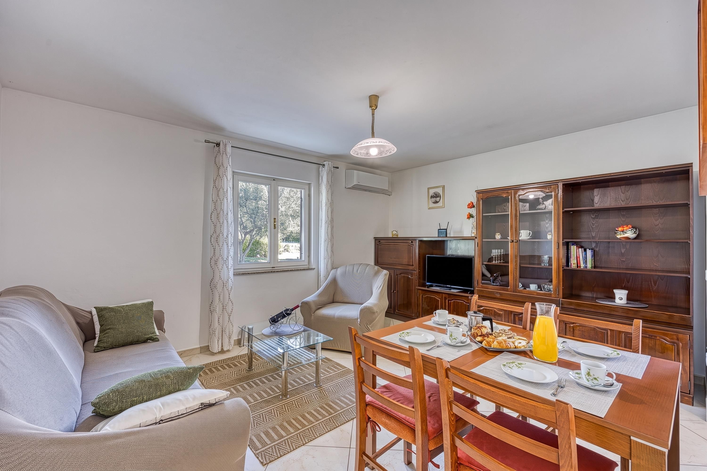 Una sala de estar con un sofá, una mesa de comedor con sillas, un televisor y un mueble con puertas de vidrio.