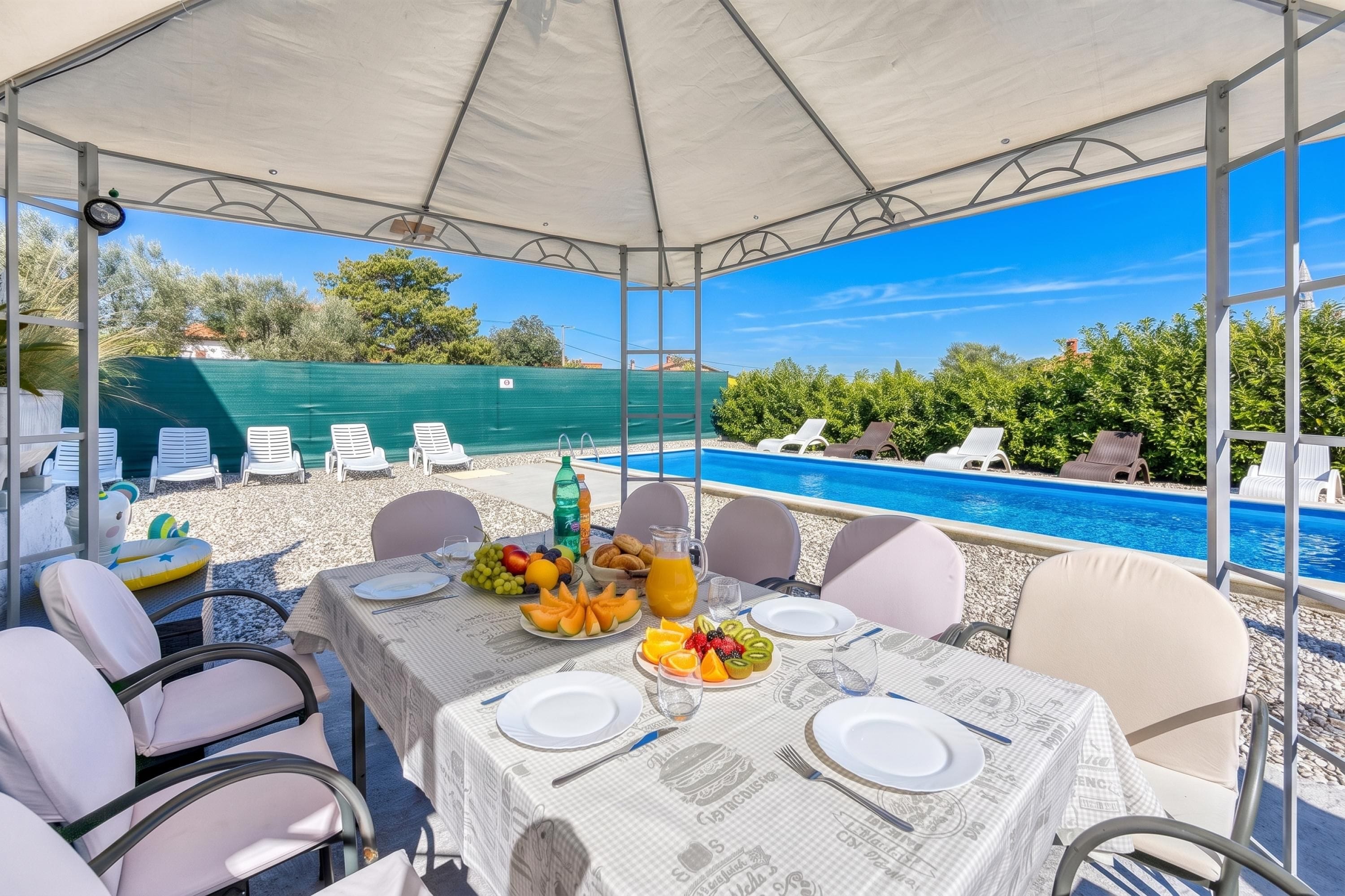 A table set for dining with a pool view, outdoor chairs, and a covered area.