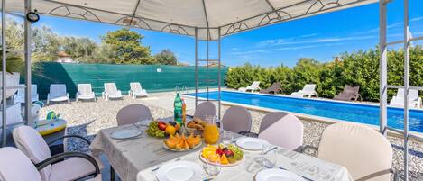 Mesa lista para comer con vista a la piscina, sillas exteriores y un área techada.