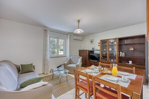 A living room with a sofa, a dining table set for breakfast, a TV, and a wooden cabinet. - Pool House Lilly (Visnjan)