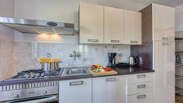 A modern kitchen with white cabinets, a stainless steel stove, and a wooden cutting board with vegetables.