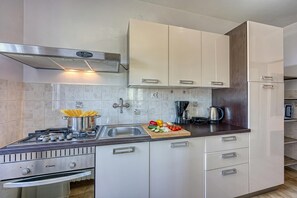 A modern kitchen with white cabinets, a stainless steel stove, and a wooden cutting board with vegetables.
