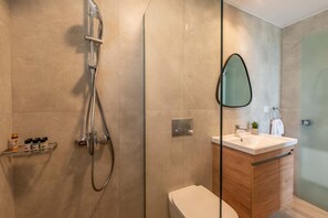 Un baño moderno con cabina de ducha de vidrio, tocador de madera con lavamanos y un inodoro.