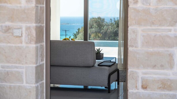 Ein modernes Wohnzimmer mit einem grauen Sofa, einem kleinen Tisch mit einer Pflanze und Meerblick durch große Fenster.
