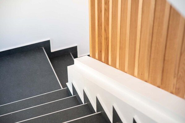 Un escalier avec des marches noires et des rampes blanches, menant à un mur en bois.