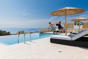 Un espace aménagé au bord de la piscine offrant une vue dégagée sur la mer, avec un fauteuil de relaxation et une petite table agrémentée d’une plante.