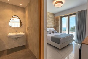 Un baño moderno con lavabo y espejo, y un dormitorio con cama y ventanas amplias.