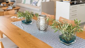 Et træspisebord med tre glasvaser med planter, en løber med mønster og et køkken i baggrunden.