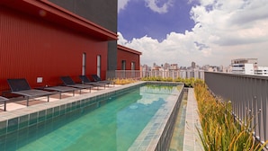 Una piscina en la azotea con sillones de descanso y vista panorámica de la ciudad.
