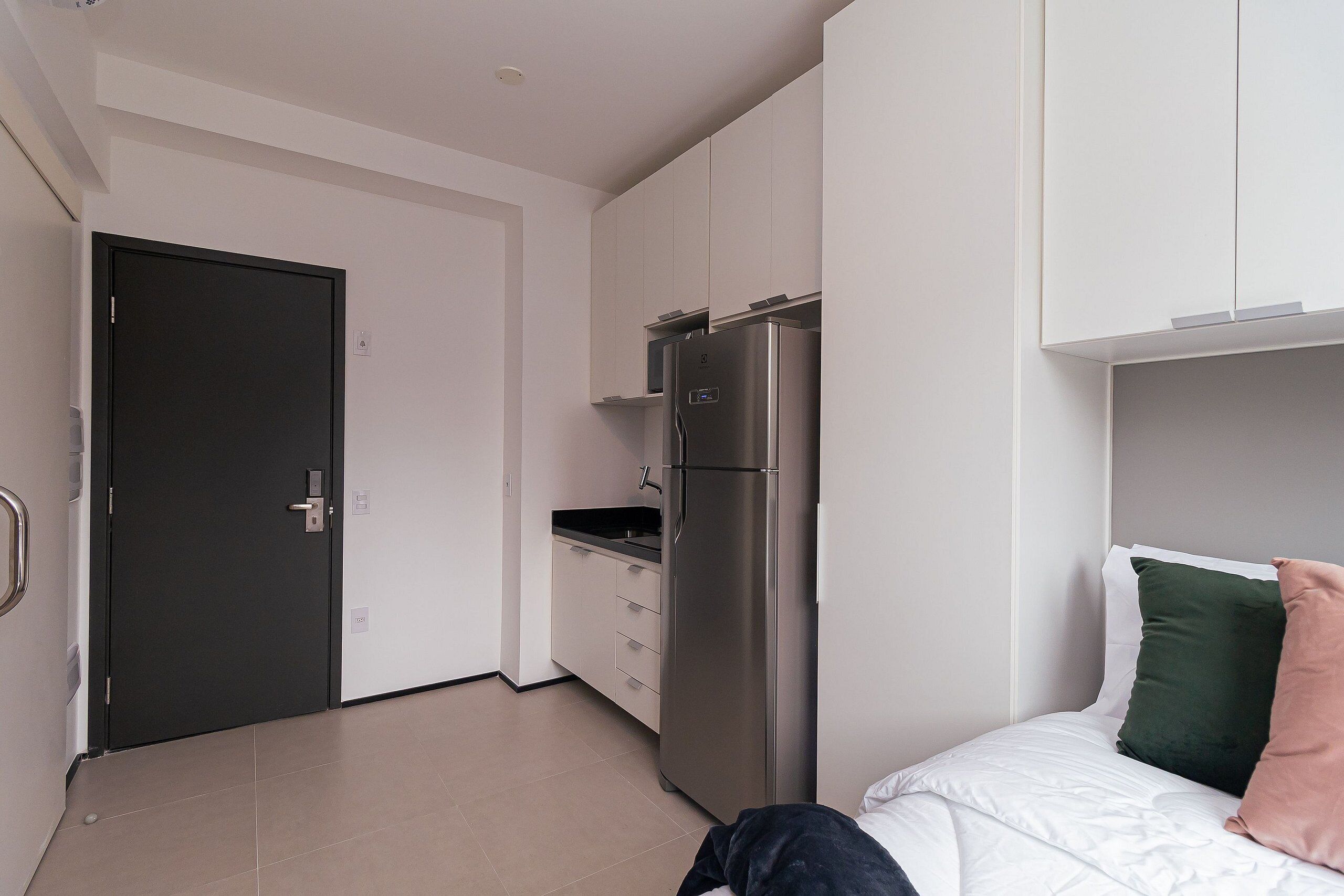 Una camera compatta con un letto, un angolo cottura e una porta che dà su un'altra stanza.