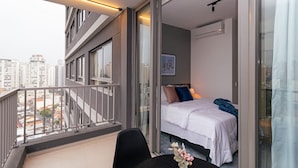 Una habitación de hotel moderna con balcón, cama con almohadas y vista a la ciudad.