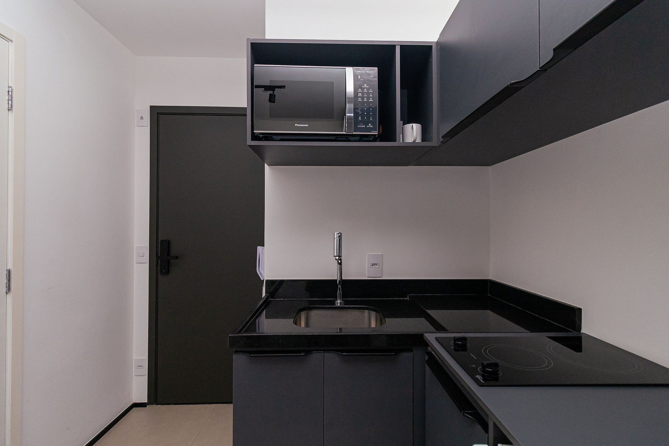 Una cocina compacta con microondas integrado, un lavamanos y una placa de cocina.