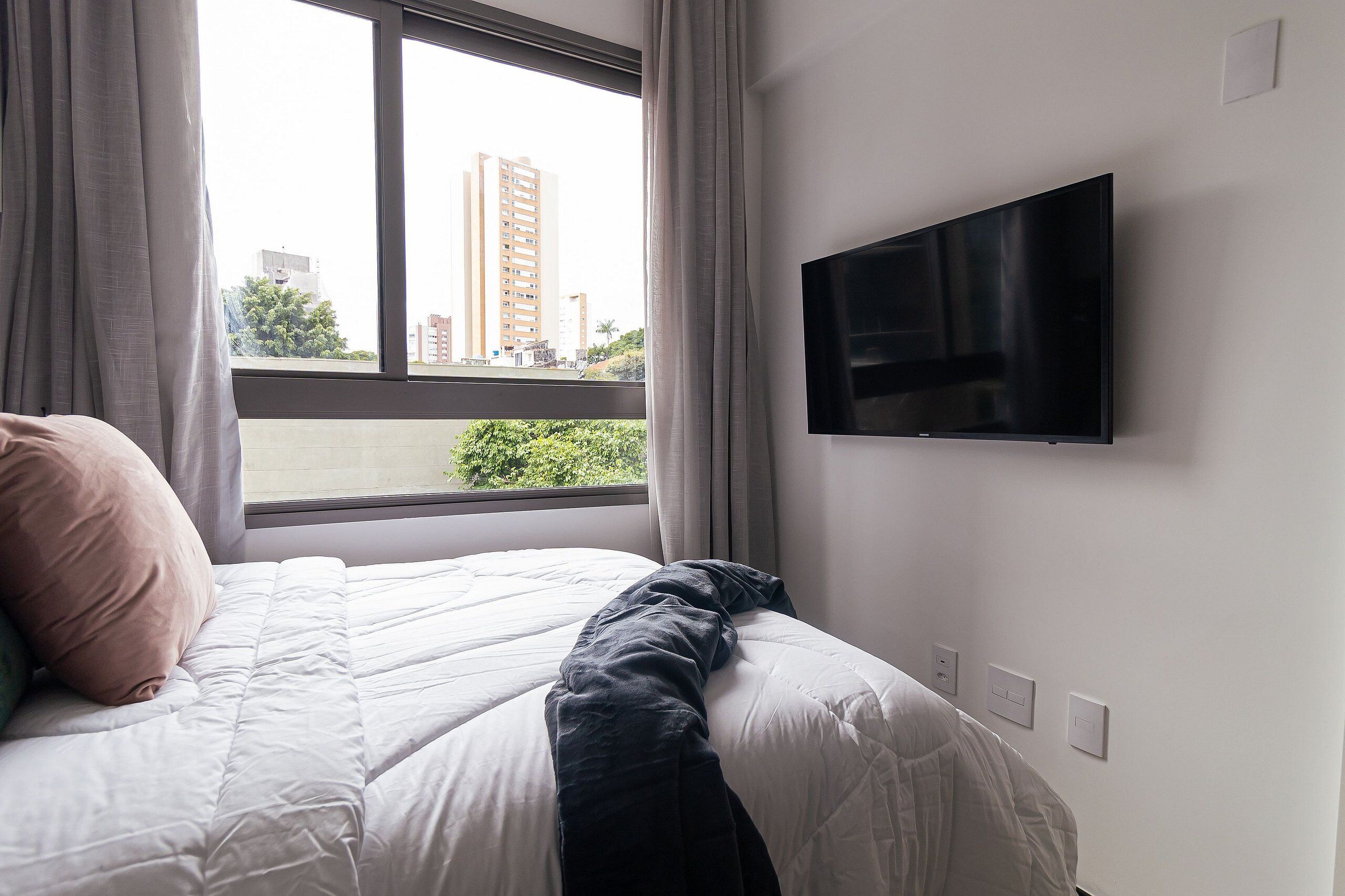 A hotel room with a bed, a TV mounted on the wall, and a window with curtains.