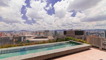 Une piscine sur le toit, offrant une vue sur la ville, entourée d’une rambarde en métal et dotée d’un sol carrelé.