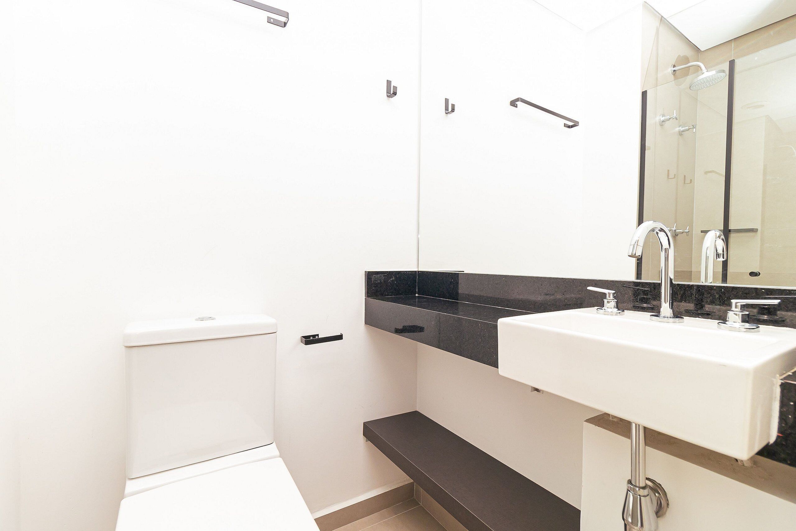 Un baño moderno con inodoro blanco, encimera negra y lavabo blanco con detalles cromados.