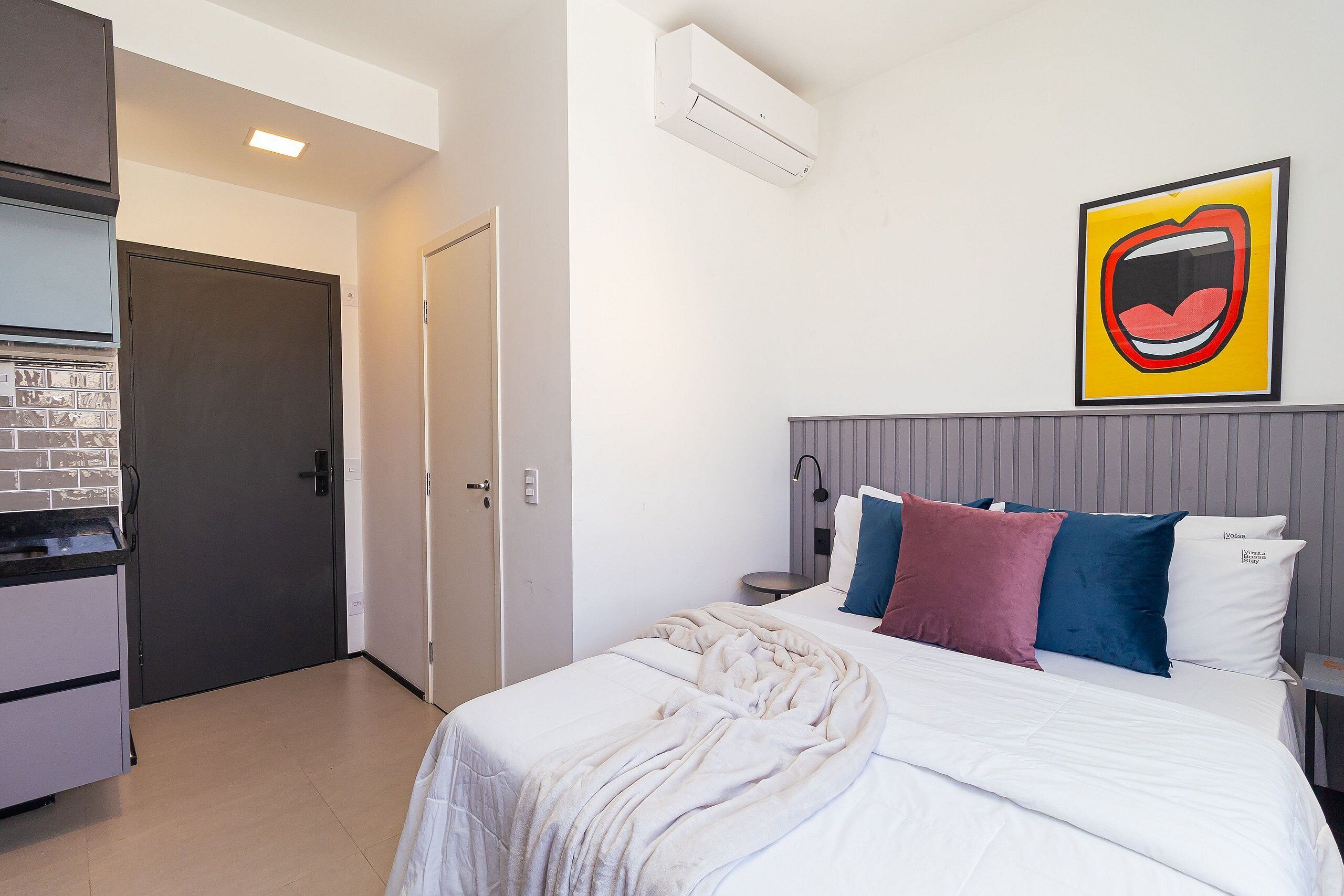 Ein Schlafzimmer mit einem Bett, Kissen, einem Nachttisch, einer Lampe und einer Wand-Klimaanlage.