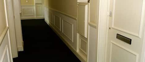 A hallway with white walls and doors, including a door with a number plate.
