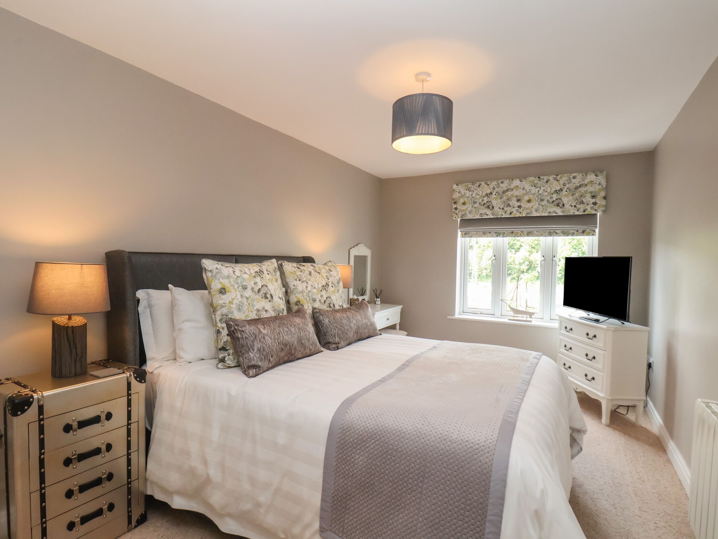A bedroom with a bed, bedside tables, a lamp, a dresser, a TV, and a window with a view.