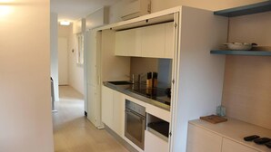 A compact kitchen with white cabinets, a stainless steel oven, and a black countertop. - Lovely Apartment in Lignano Sabbiadoro (Lignano Sabbiadoro)