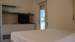 A bedroom with a bed, a television on a stand, and a door leading to a balcony. - Lovely Apartment in Lignano Sabbiadoro (Lignano Sabbiadoro)
