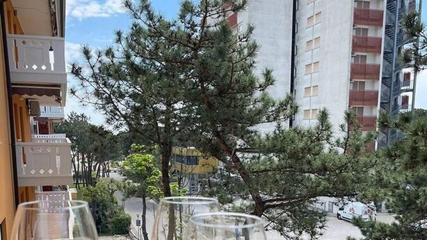 A balcony with three wine glasses, overlooking a parking area and trees. - Lovely Apartment in Lignano Sabbiadoro (Lignano Sabbiadoro)