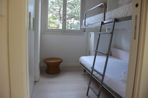 A bunk bed room with a window, a wicker stool, and a radiator.
