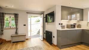 A modern kitchen with grey cabinets, a built-in microwave, and a kettle. There's a fluffy rug on the floor and a window with curtains. - The Office (Telford)