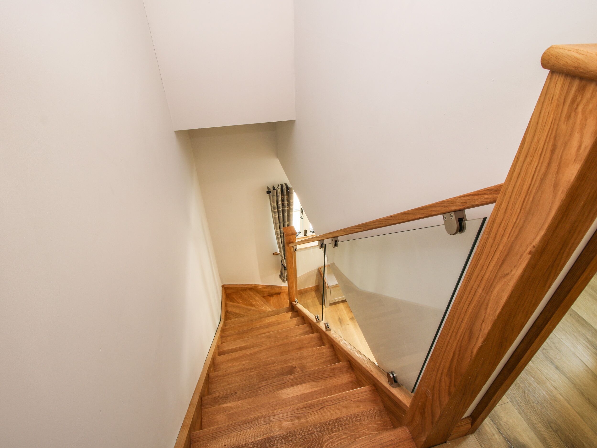 A wooden staircase with a glass railing leading to a landing.