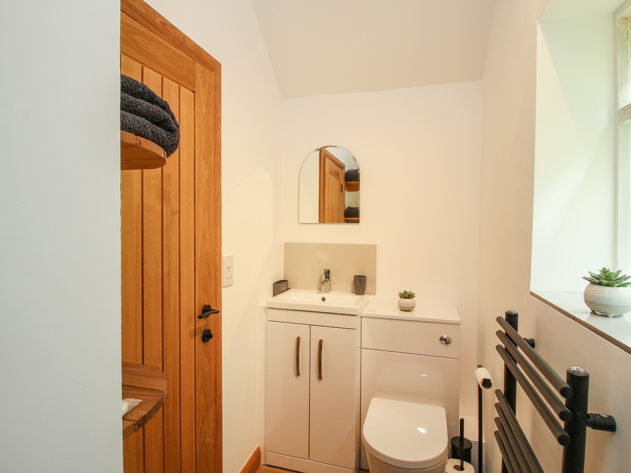 Une petite salle de bain avec une porte en bois, un lavabo blanc, des toilettes et un miroir au-dessus du lavabo.
