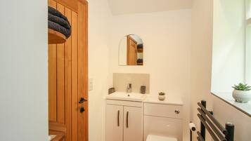 Une petite salle de bain avec une porte en bois, un lavabo blanc, des toilettes et un miroir au-dessus du lavabo.