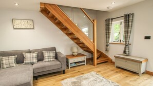 A modern living room with a grey sectional sofa, a wooden staircase, a fluffy rug, and a window with curtains. - The Office (Telford)