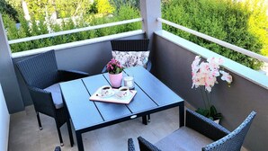 A balcony with a table and chairs, a potted plant, and a view of a green landscape with buildings. - Apartment Near Beach With the Balcony (Podstrana)
