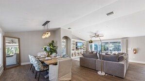 A modern living room with a dining area, a grey sofa, a floor lamp, and a ceiling fan.