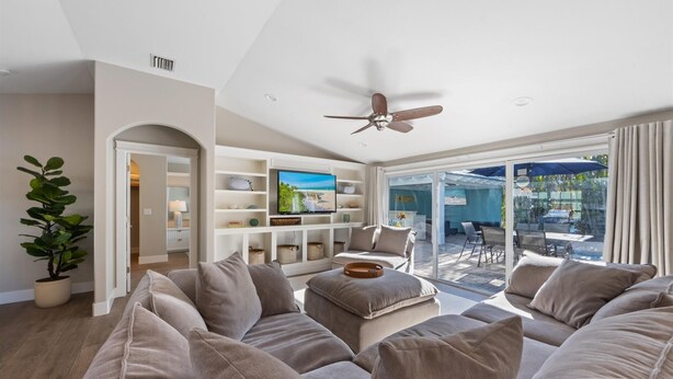 A modern living room with a beige sofa, a television, and a ceiling fan.