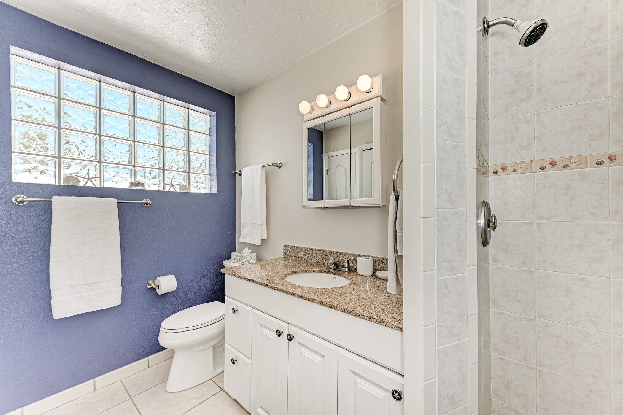 Un baño con pared azul, inodoro blanco, lavabo con espejo y ducha.