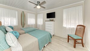 A bedroom with two beds, a ceiling fan, a dresser, a TV, and a chair.