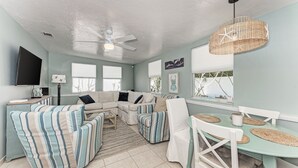 A living room with a sectional sofa, striped armchairs, a dining table with placemats, and a ceiling fan.