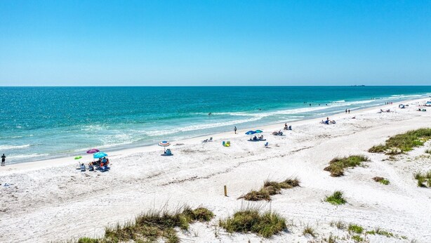 A beach with white sand, clear blue water, and several umbrellas.