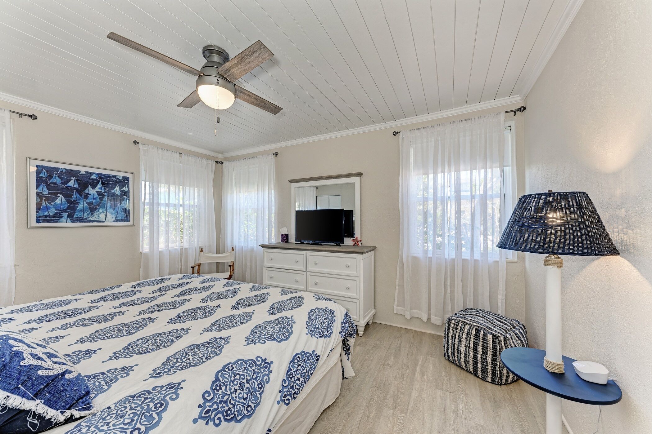 A bedroom with a bed, a dresser, a television, a ceiling fan, and a lamp.