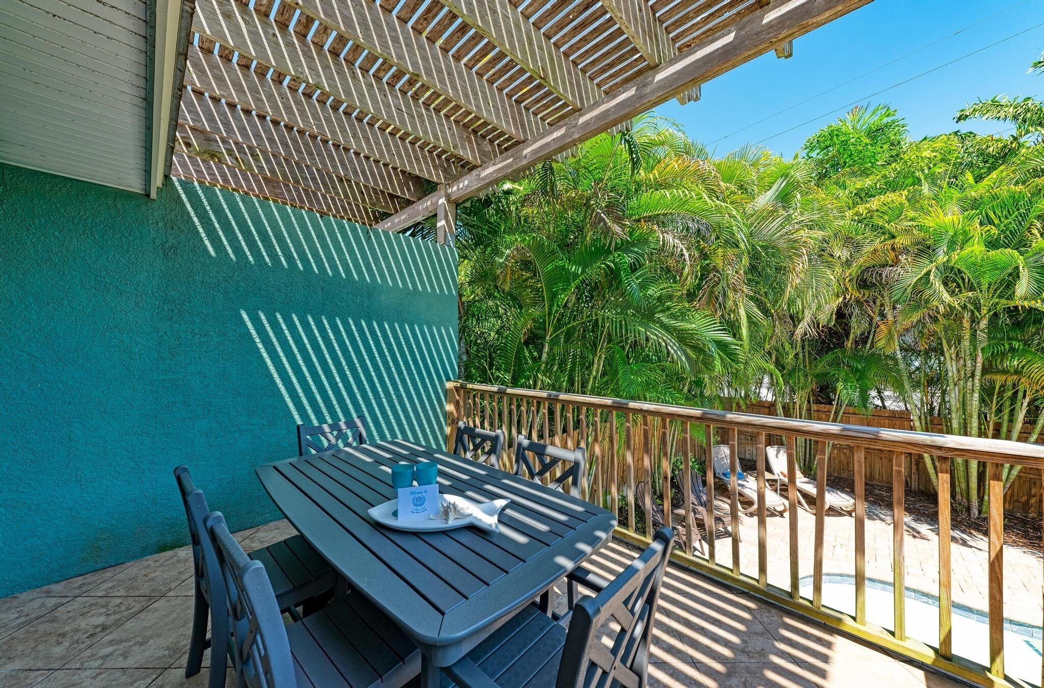 A patio with a table and chairs, a wooden railing, and a view of palm trees.