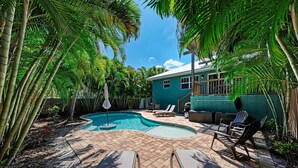 A backyard with a swimming pool, lounge chairs, and a house.