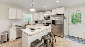 A modern kitchen with white cabinetry, stainless steel appliances, and a central island with stools.