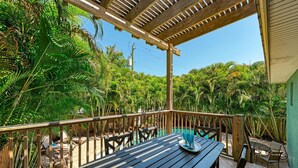 A wooden deck with a table and chairs, surrounded by lush tropical vegetation.
