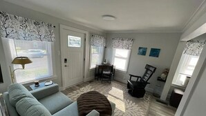 A living room with a sofa, a coffee table, a dining table with chairs, and a fireplace. - Perfectly Small House (Xenia)