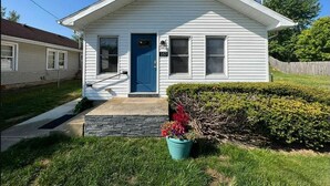 A single-story house with a blue door, a number '357' on the door, and a small front porch. - Perfectly Small House (Xenia)