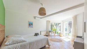 A bedroom with a bed, a bedside table, a lamp, a window, and a view of the outdoors.